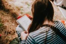 One of the participants of the Green Academy 2020 is sitting on the grass and taking notes