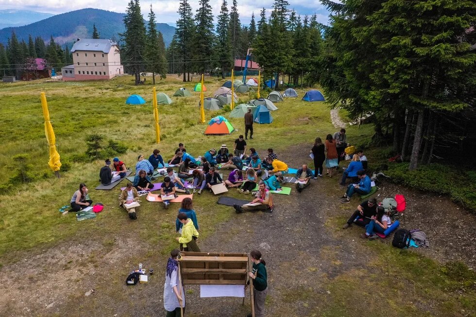 Green Camp participants are sitting on pads next to the campsite and following the trainers’ guidelines