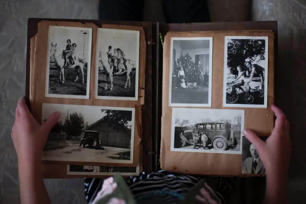 Фото згори, як людина на колінах тримає розгорнутий старий фотоальбом