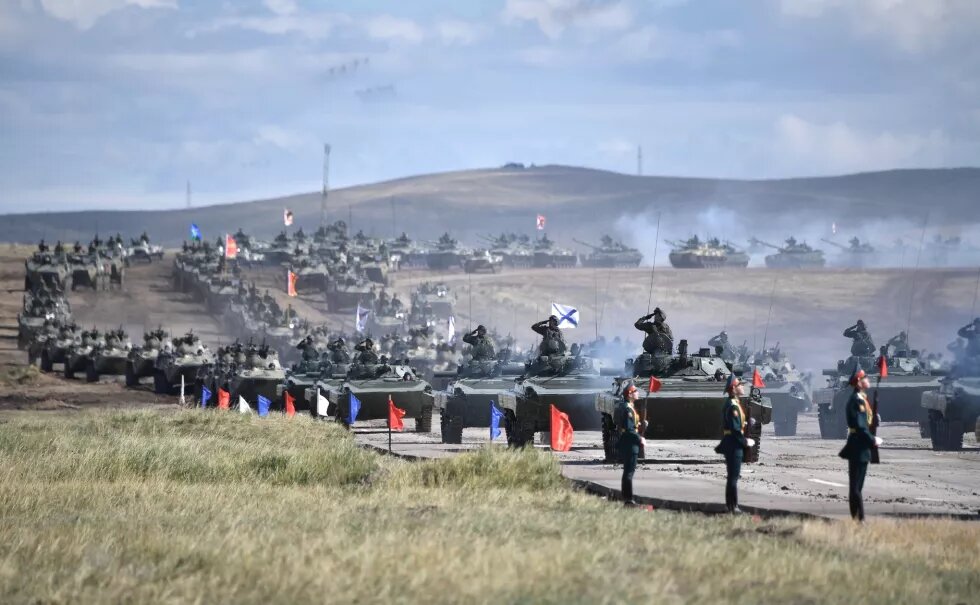 Armed vehicles are moving across grass-land amid a parade