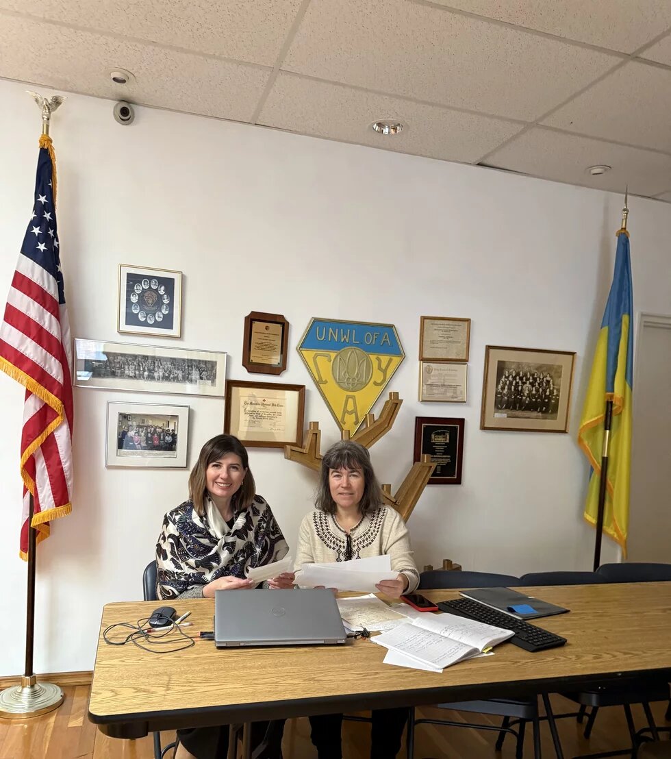 Дві жінки в кабінеті на фоні прапору США та України 