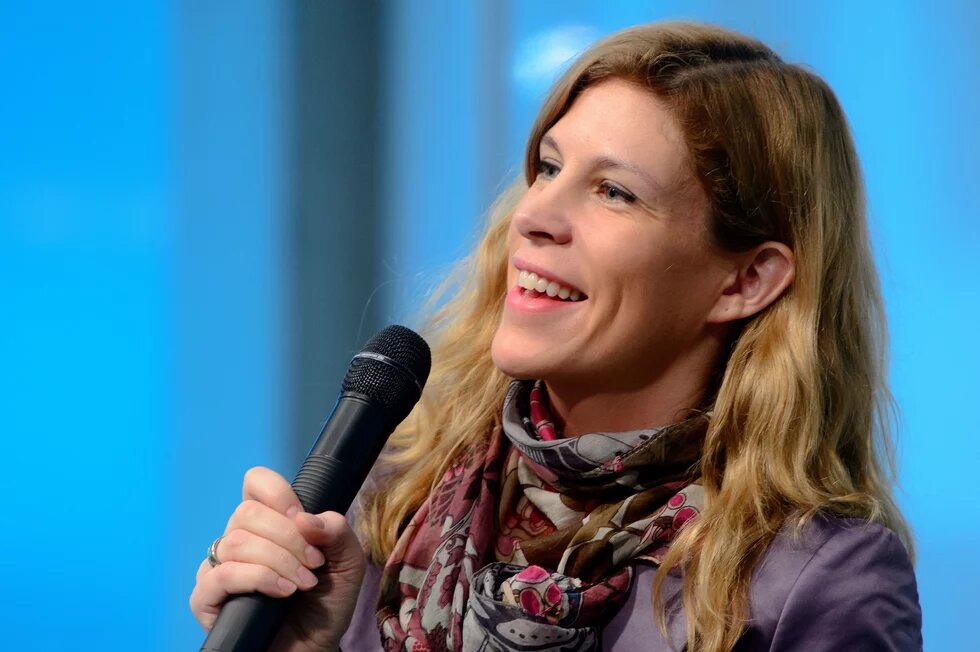 A blond woman smiling and speaking with microphone - Antonie